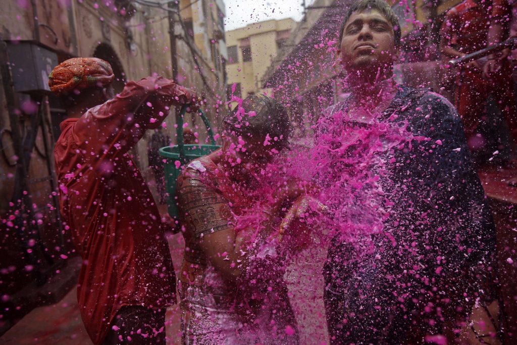 People splash coloured water on a woman as she walks in a lane during Holi celebrations in Vrindavan