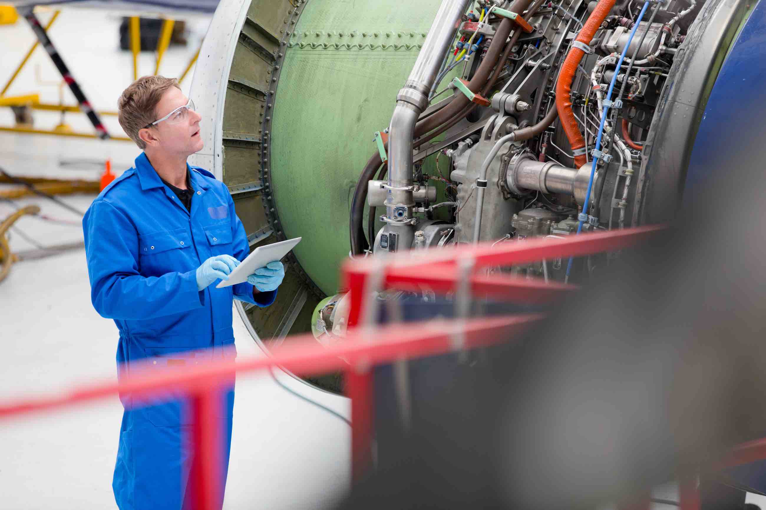 Engineer with digital tablet inspecting engine of passenger jet in hangar